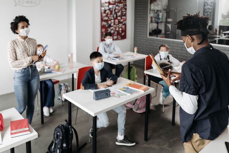 A diverse group of students and a teacher wearing masks in a classroom.