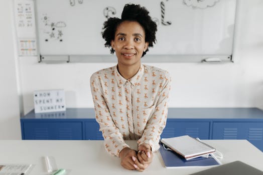 African American woman smiling confidently at desk with notebook in bright office setting.