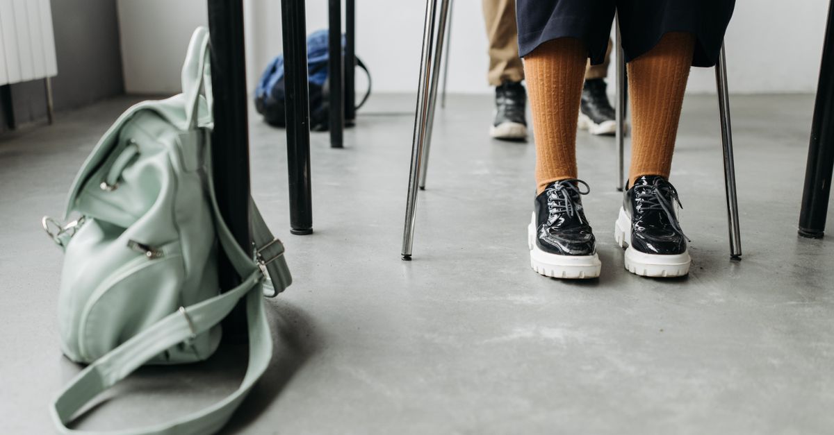 Close-up of stylish shoes and a backpack on the floor next to a school desk indoors.
