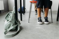Close-up of stylish shoes and a backpack on the floor next to a school desk indoors.