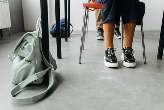 Close-up of stylish shoes and a backpack on the floor next to a school desk indoors.