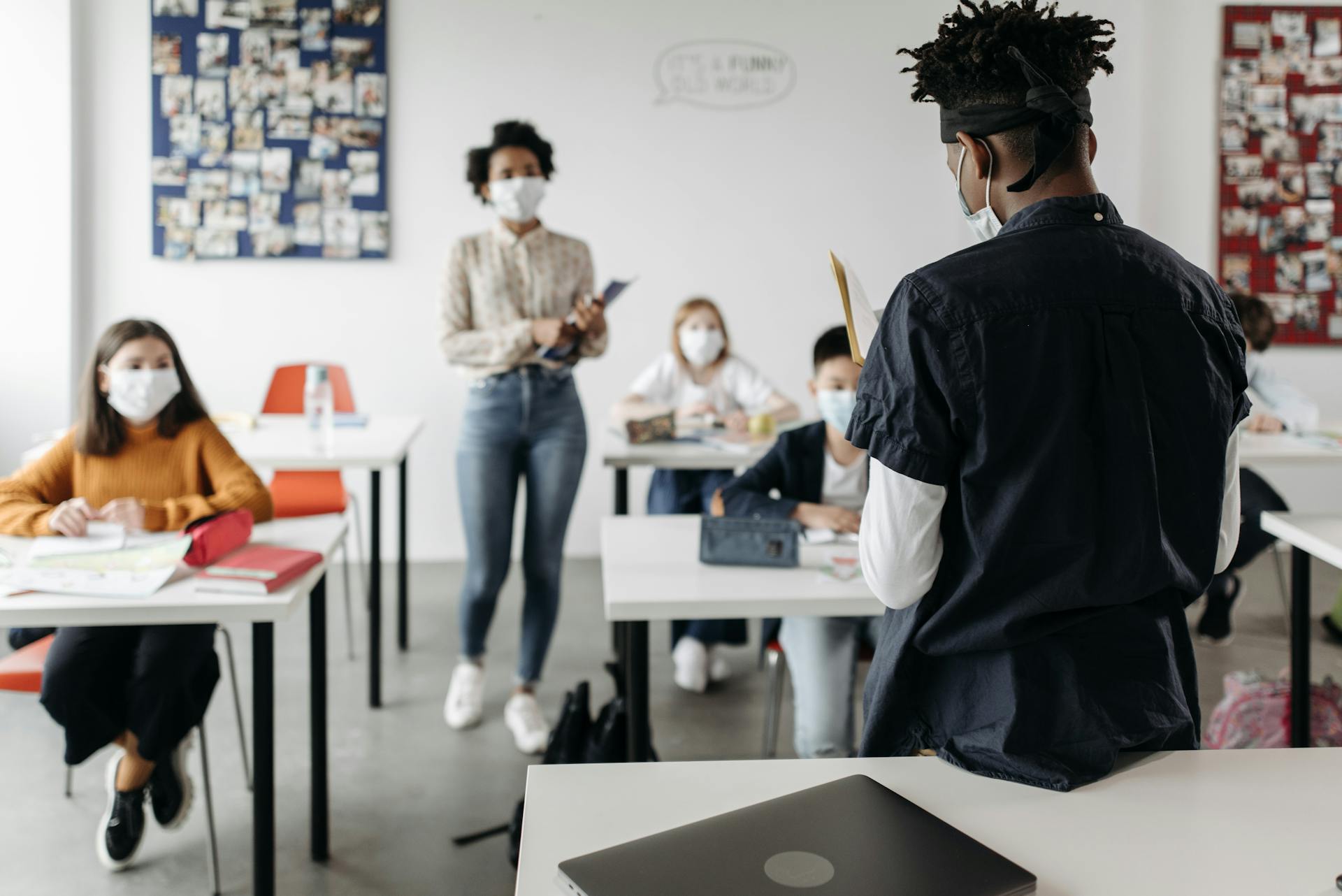 A teacher and students wearing masks in a classroom setting, adapting to new normal education during the pandemic.