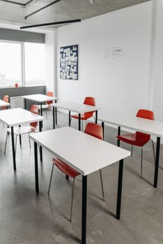 Contemporary classroom interior with red chairs and white desks arranged in rows.