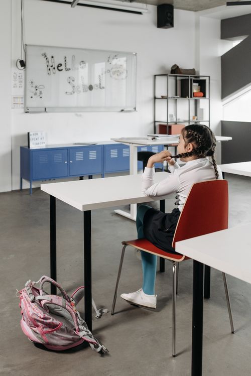 Free Girl sitting in classroom facing whiteboard with 'Hello School' on it. Stock Photo