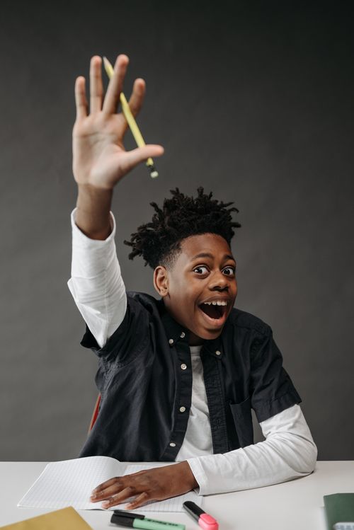 Free An excited student raises his hand during a classroom activity, showcasing eagerness to participate. Stock Photo