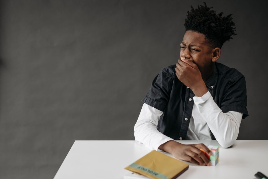 A discouraged young person sitting at a desk with an open notebook and laptop, resting their head on their hand, looking tired of studying English