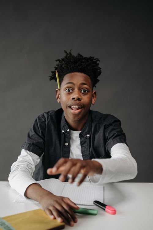 Free A young student with dreadlocks smiling and sitting at a desk, with a gray background. Stock Photo