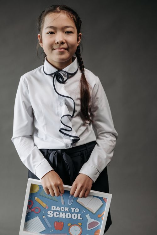 Free Young girl smiling in uniform holding a back to school poster with educational icons. Stock Photo