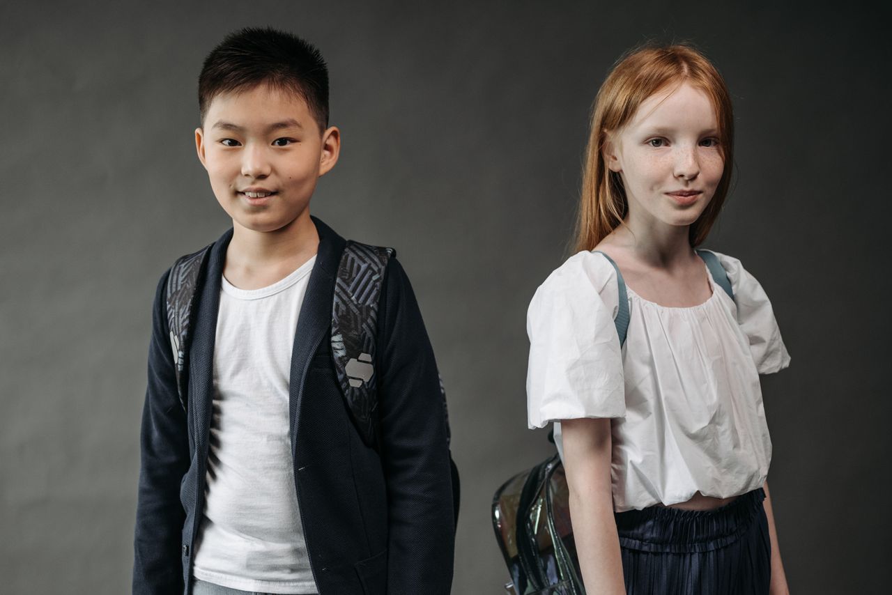 two schoolchildren smiling with backpacks in a studio setting