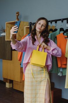Stylish woman taking a selfie with a yellow bag in a modern boutique. Trendy clothing and personal style.