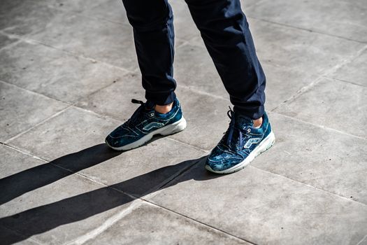 A person wearing stylish sneakers stands on a sunlit urban pavement, casting a distinct shadow.