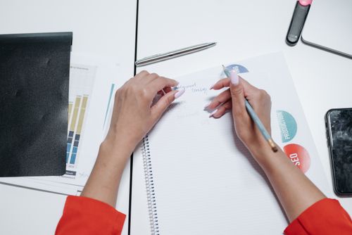 Free Close-up view of hands writing on a notepad with printed charts and graphs. Stock Photo
