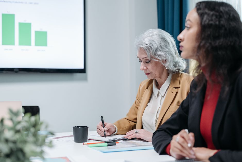 Businesswomen engaged in a collaborative office meeting, taking notes and analyzing data.