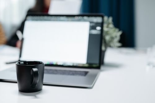 Free A black coffee mug on an office desk with a blurred laptop in the background. Stock Photo