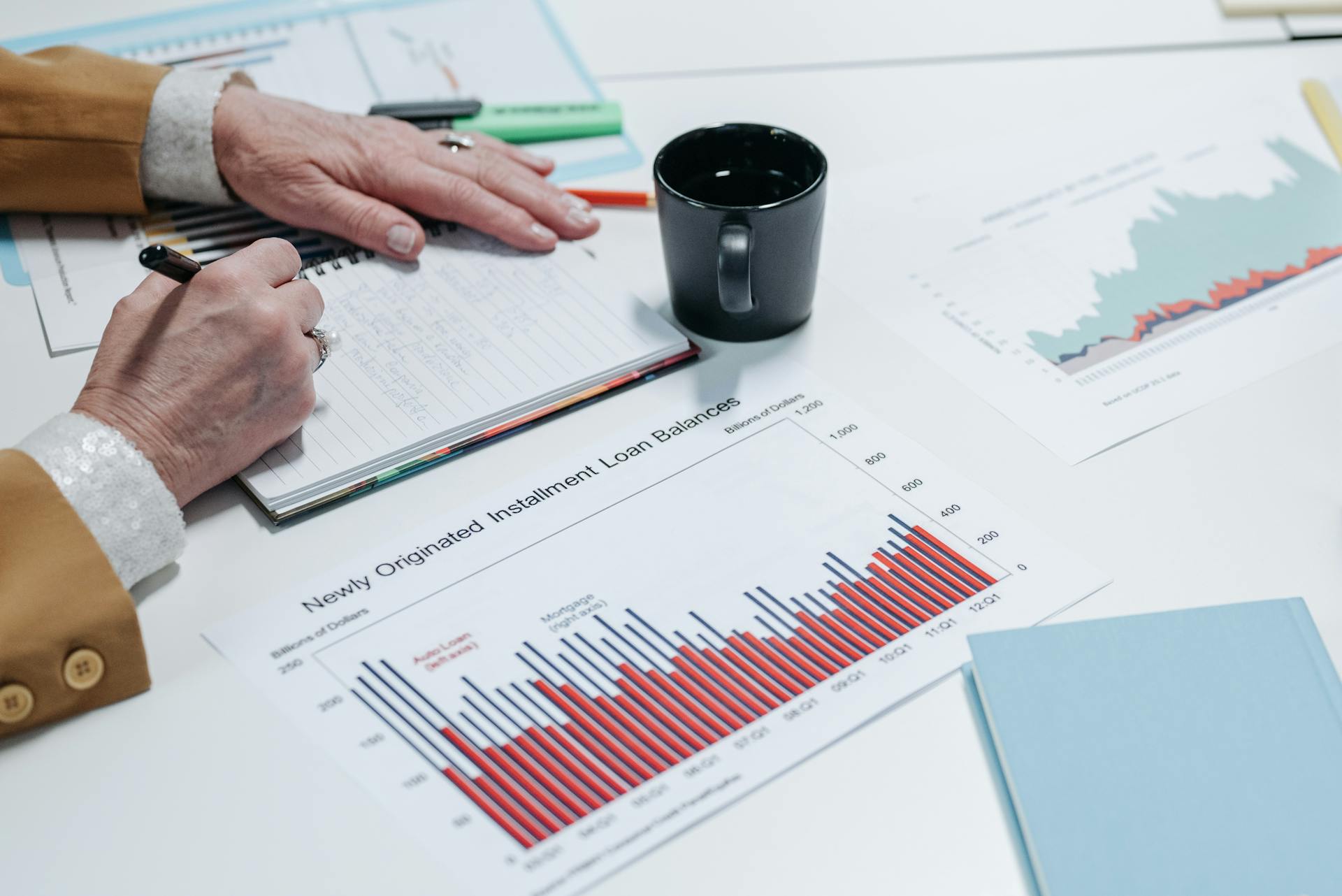 Close-up of a person analyzing financial charts and taking notes in an office setting.