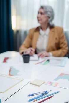 Senior businesswoman at white desk with office supplies during a meeting.