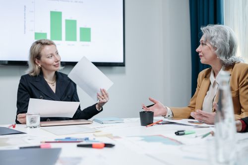 Free Two businesswomen engaged in a meeting discussing charts in an office setting. Stock Photo