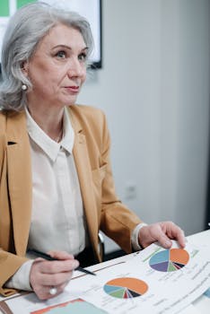 Senior woman in blazer reviews business charts with focus and concentration.