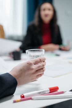 Hand holding a water glass during a business meeting. Office setting with focus on teamwork.