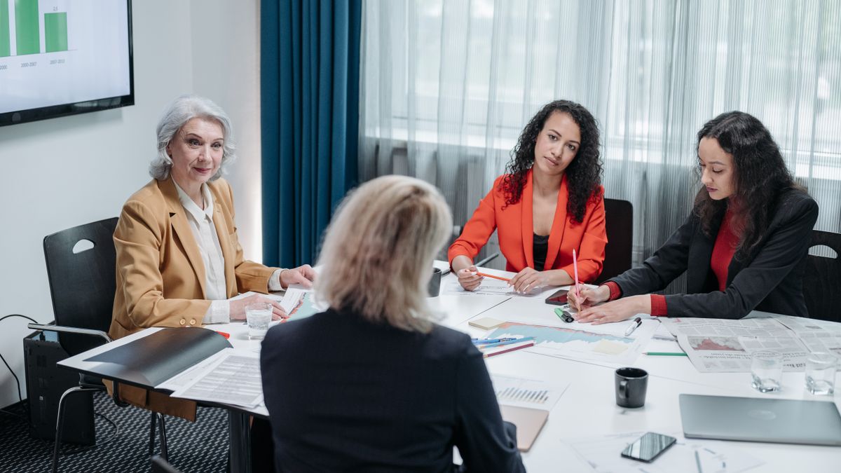 Four businesswomen collaborating in a meeting room, discussing strategies and analyzing data charts.
