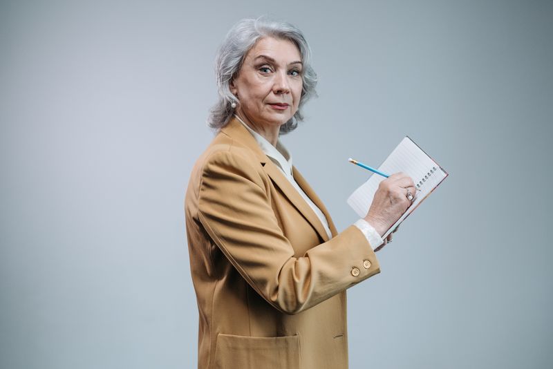 Frau mit grauen Haaren im beigen Blazer macht sich Notizen