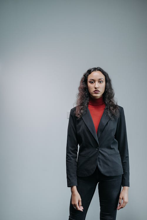 Serious Woman in Black Blazer Standing Against Gray Background