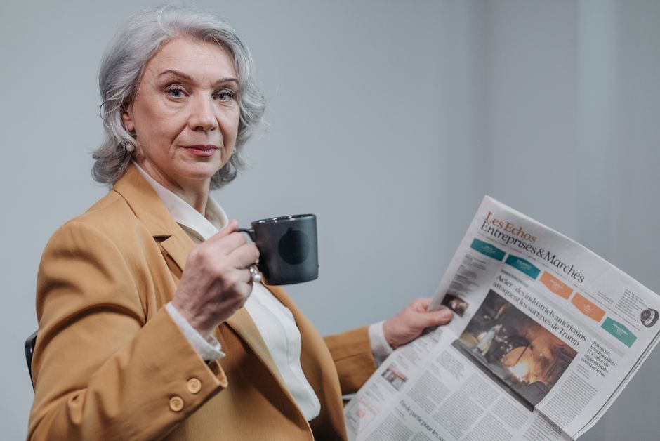 Mujer de negocios senior segura sosteniendo café y leyendo un periódico en interiores.