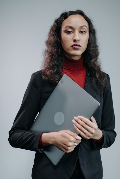 Free Serious Woman in Black Blazer Holding a Laptop while Looking at Camera Stock Photo