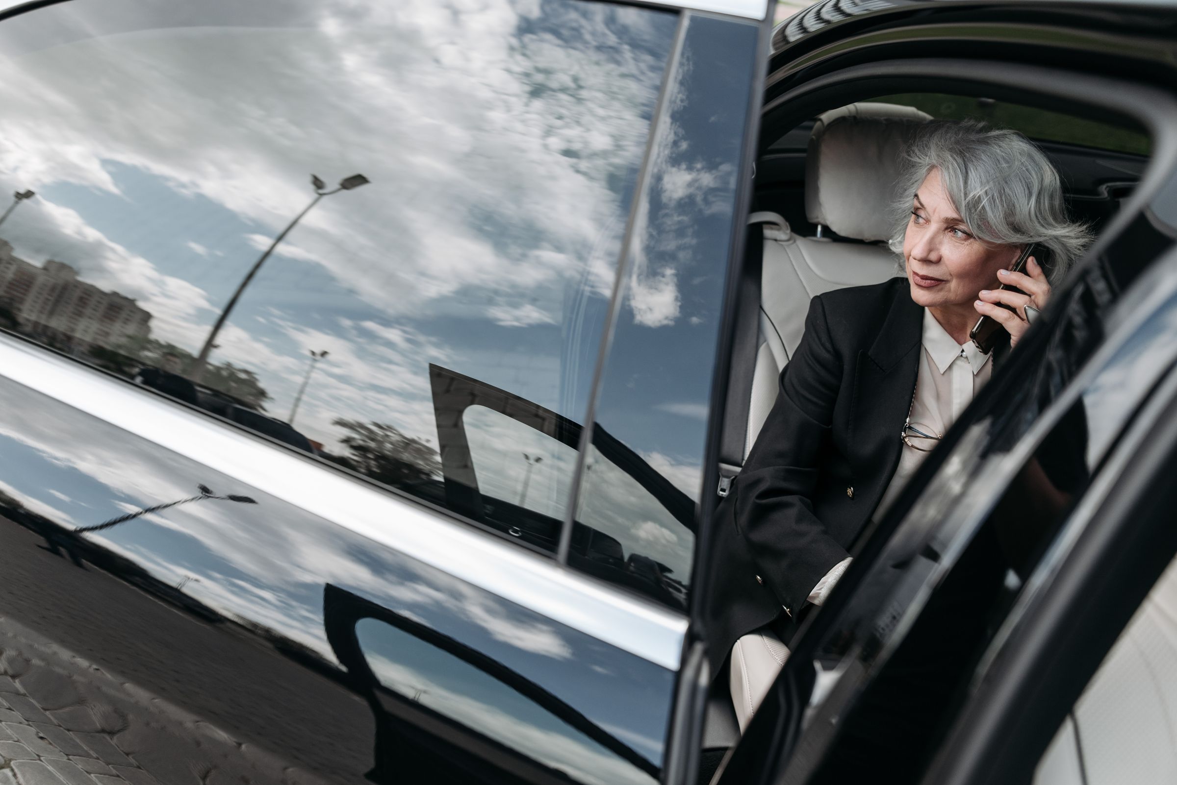 Elegant high-class woman stepping out of a luxury Mercedes-Benz vehicle with chauffeur assistance, representing premium executive transportation, luxury travel, and VIP black car service.