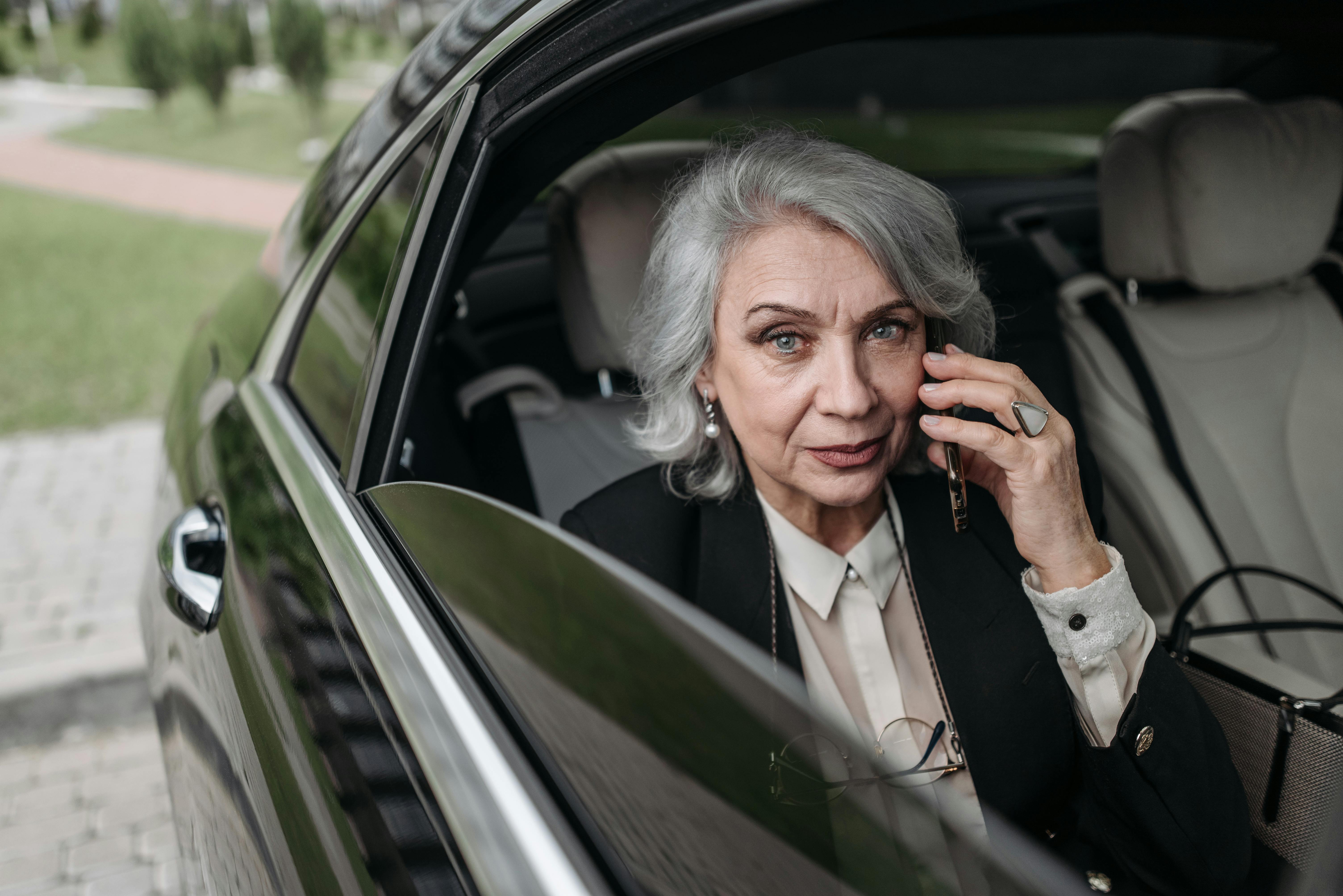 Confident senior businesswoman communicating on smartphone while seated in a luxurious car interior.