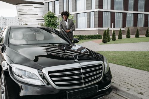 Free Confident man in suit next to a luxury car, embodying success in cityscape. Stock Photo