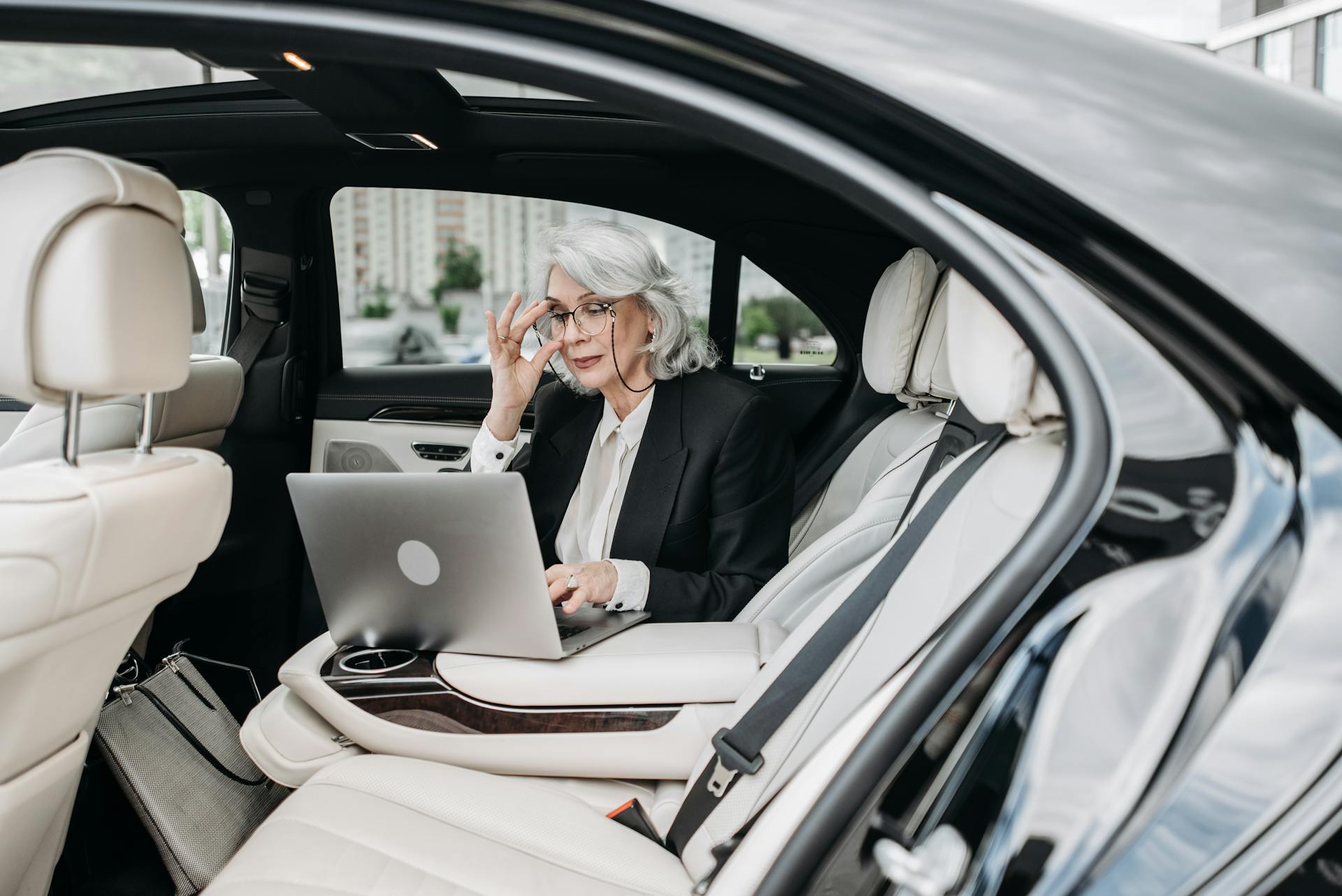 Professional woman in a luxury car using a laptop, representing modern business lifestyle.