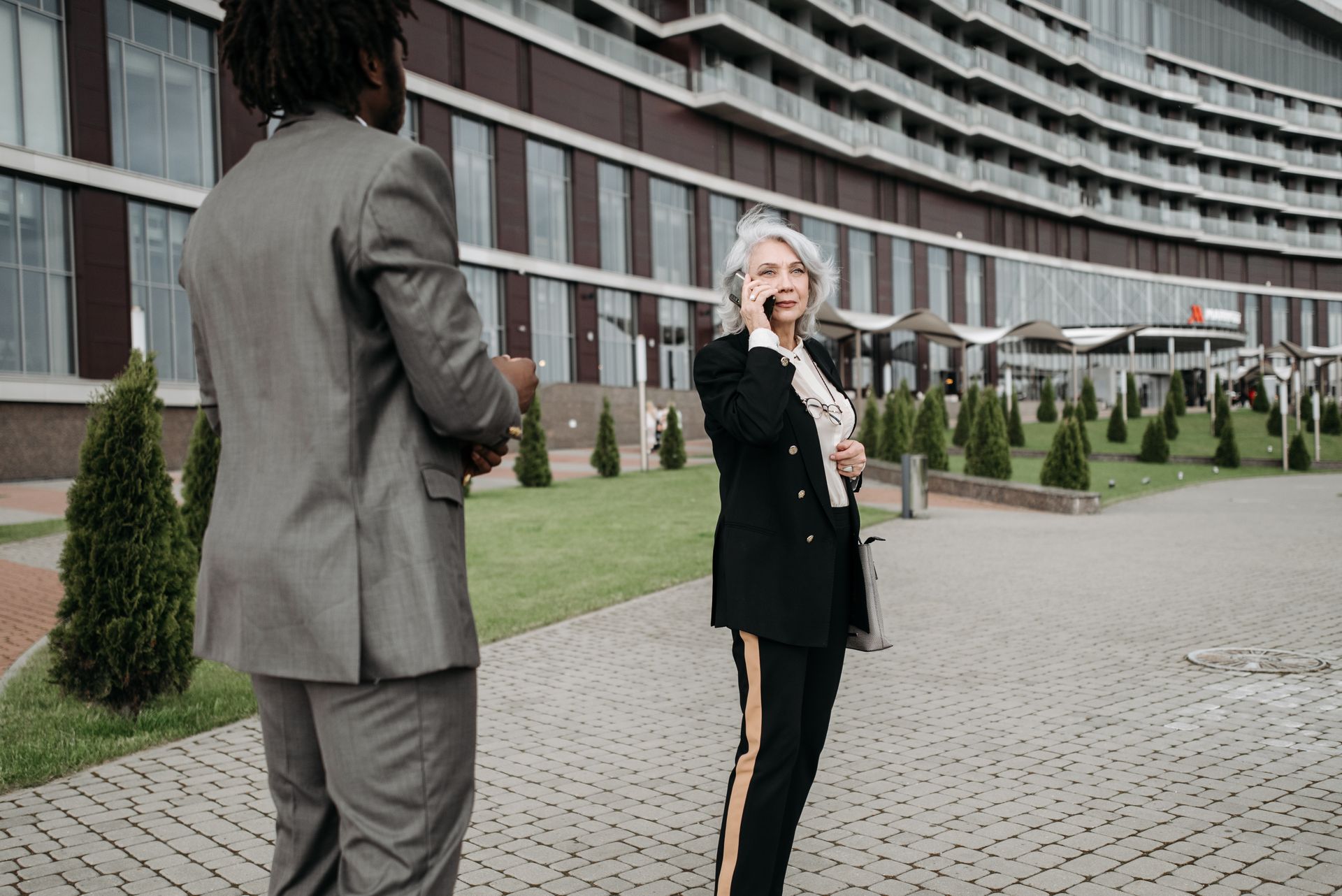 Two business professionals in outdoor urban setting, using smartphones for communication.