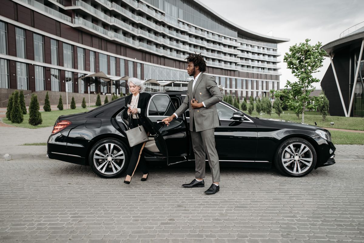 Chauffeur assisting a business traveller stepping out of a luxury sedan