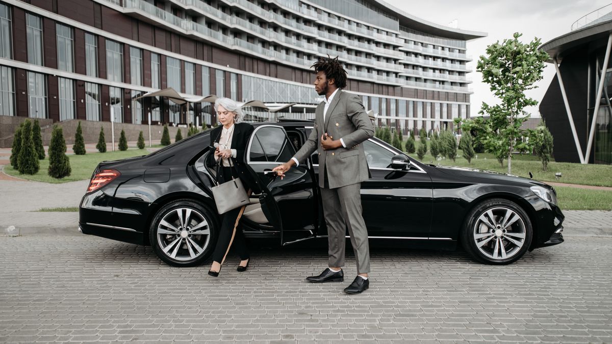 Chauffeur assisting a traveller beside a luxury car
