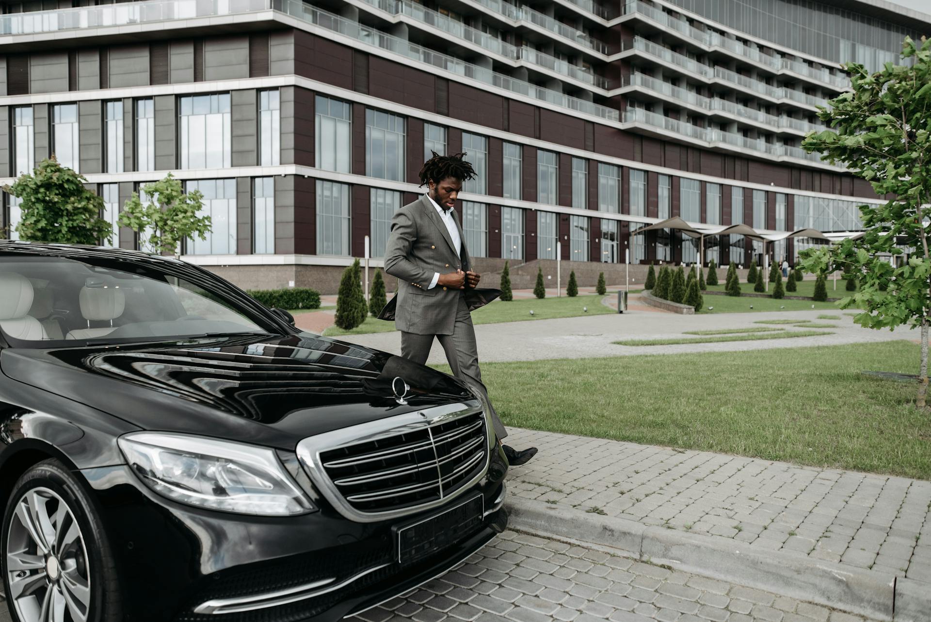 African American businessman in suit walking past luxury car in modern cityscape.