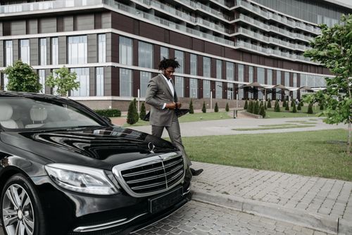 Free African American businessman in suit walking past luxury car in modern cityscape. Stock Photo