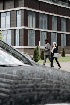 Two adults in business attire walking outside a modern office building, talking.
