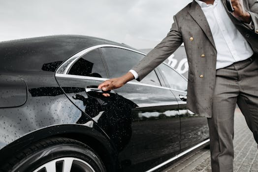 A man in a suit opens a luxury car door under raindrops on stone pavement.