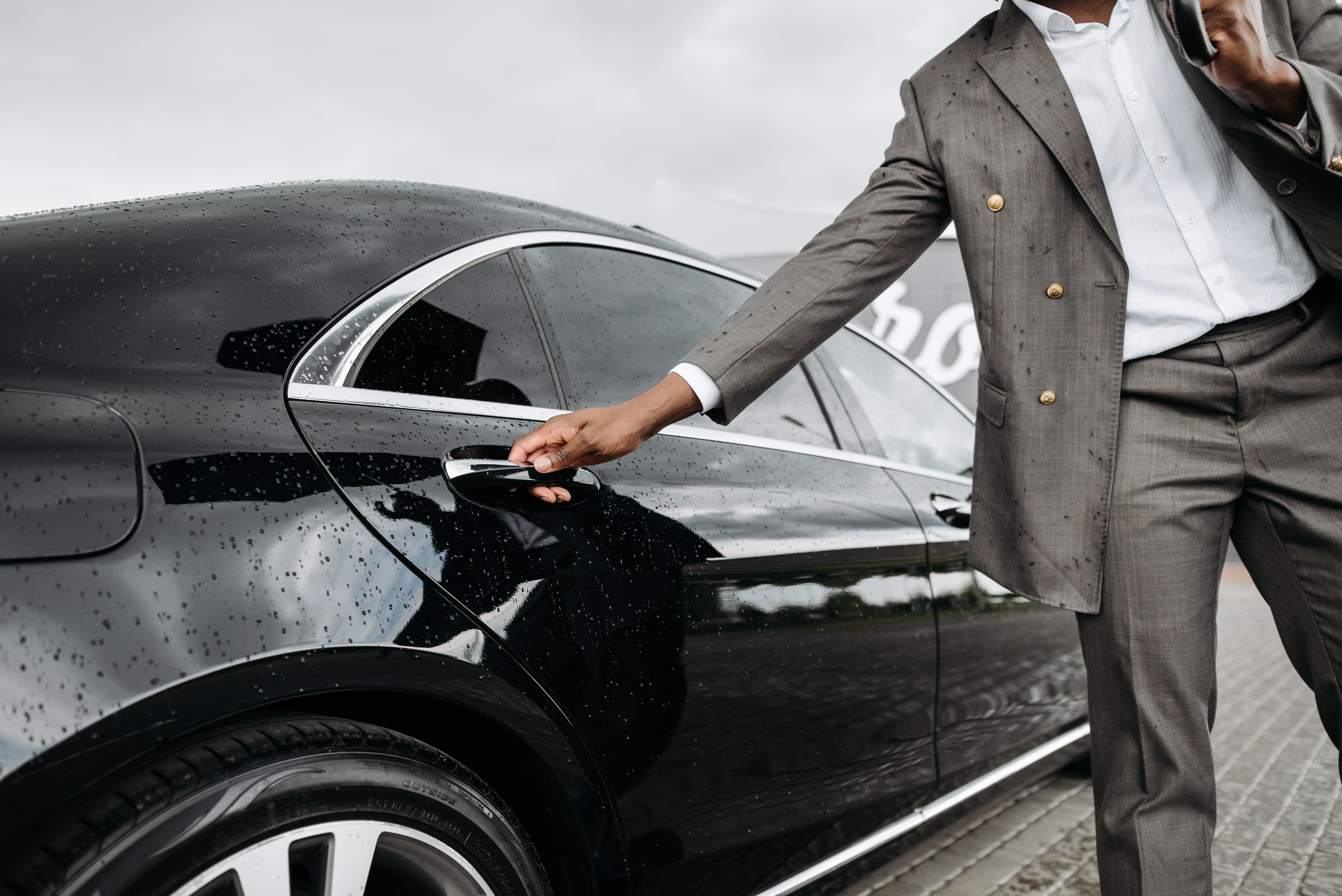 A professional chauffeur waiting beside a luxury car
