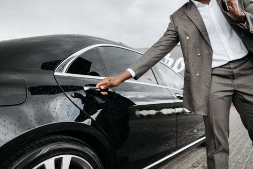 Free A man in a suit opens a luxury car door under raindrops on stone pavement. Stock Photo
