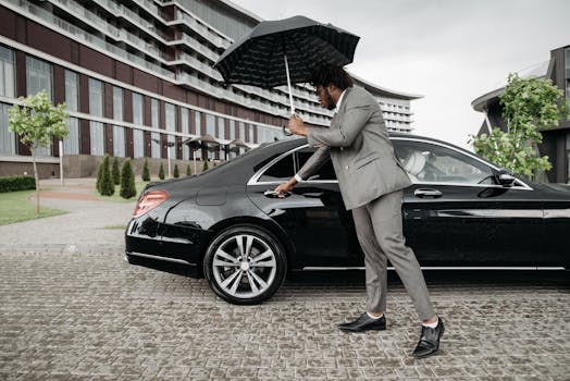 Elegant man in suit opens car door under umbrella by modern building on rainy day.