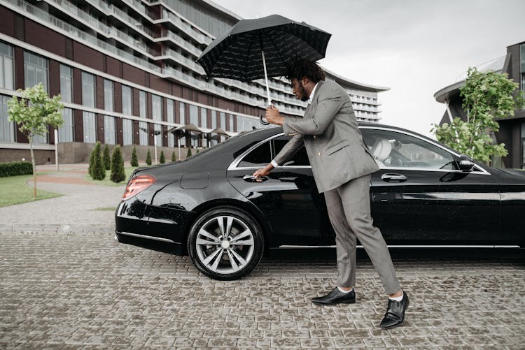 A Man Opening A Car Door While Holding An Umbrella 