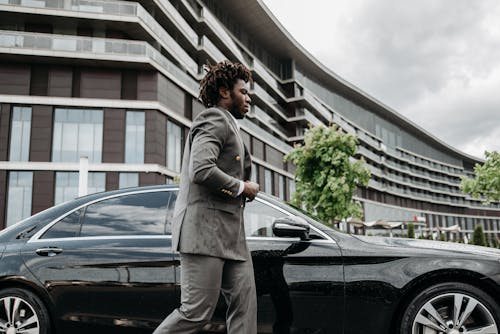 Man in Gray Suit Walking Beside Black Car