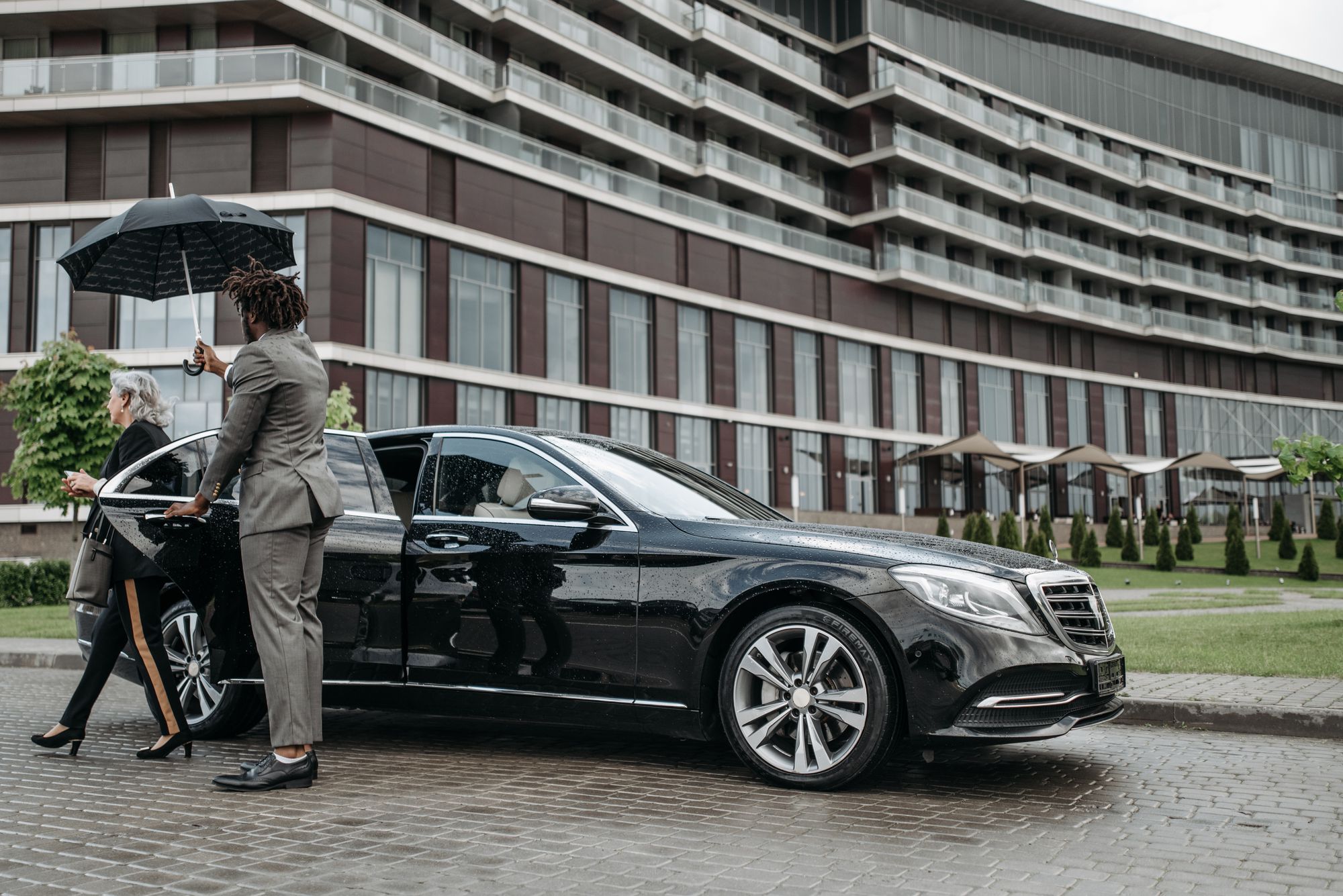 Driver holding an umbrella over a client as she walks to a black sedan