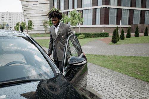 Free Man in a gray suit opening a black car door in an urban setting. Stock Photo