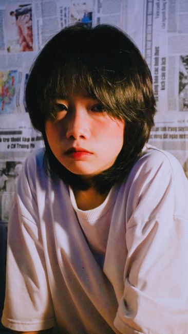 A thoughtful portrait of a young woman with dark hair in a white shirt against a newspaper backdrop.
