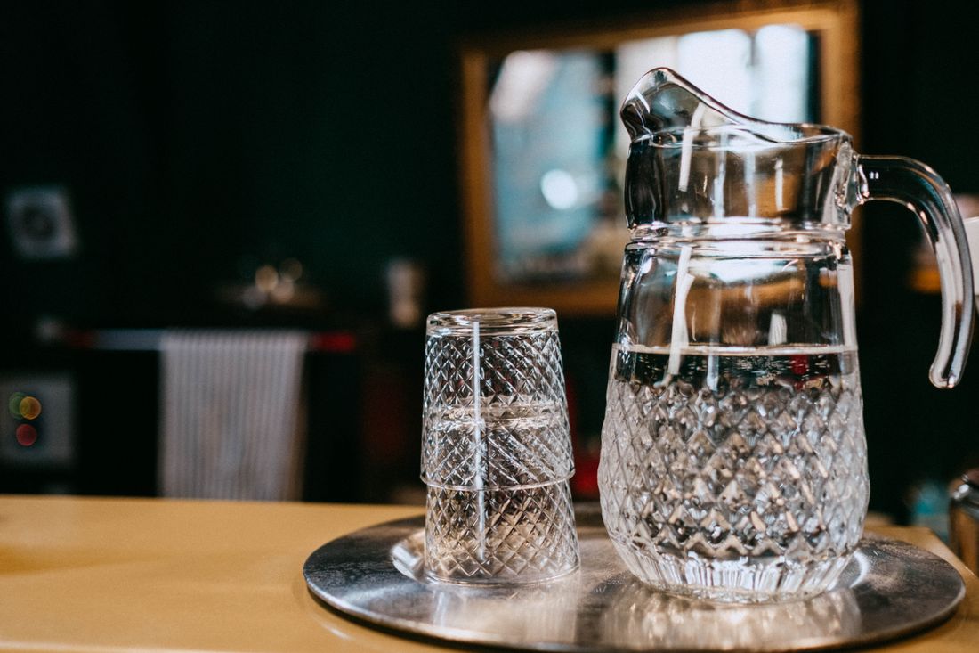 Diamond-cut glass water pitcher and stacked tumblers on a metal tray