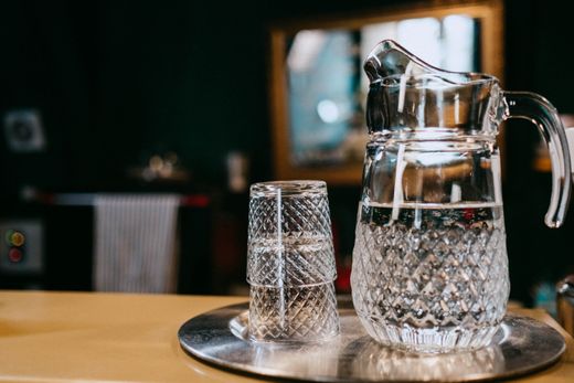 Diamond-cut glass water pitcher and stacked tumblers on a metal tray
