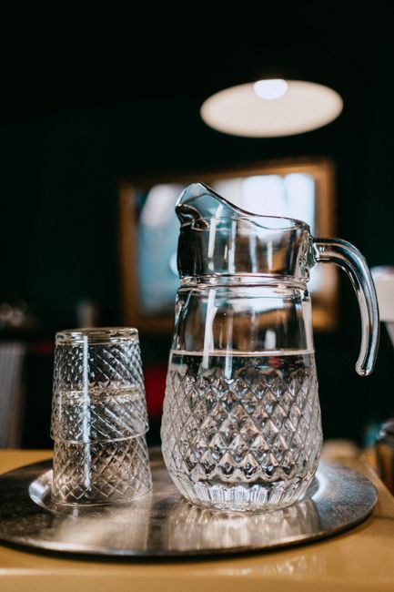 Fotomural Un primer plano de una jarra de vidrio transparente y vasos con patrones intrincados, colocados en una bandeja en interiores.